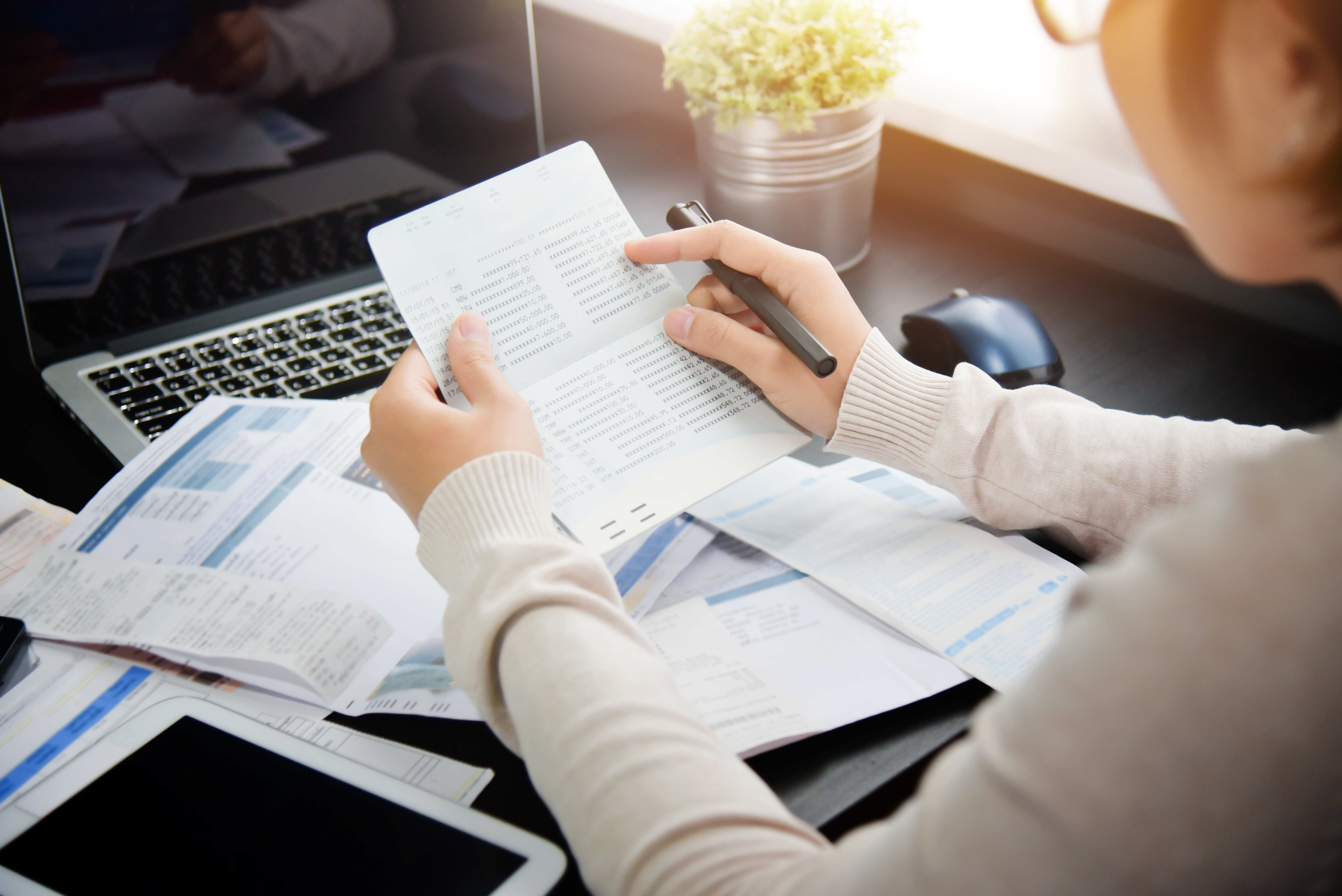 Asian woman looking to saving account book and calculating her monthly expenses with calculator. Debt.